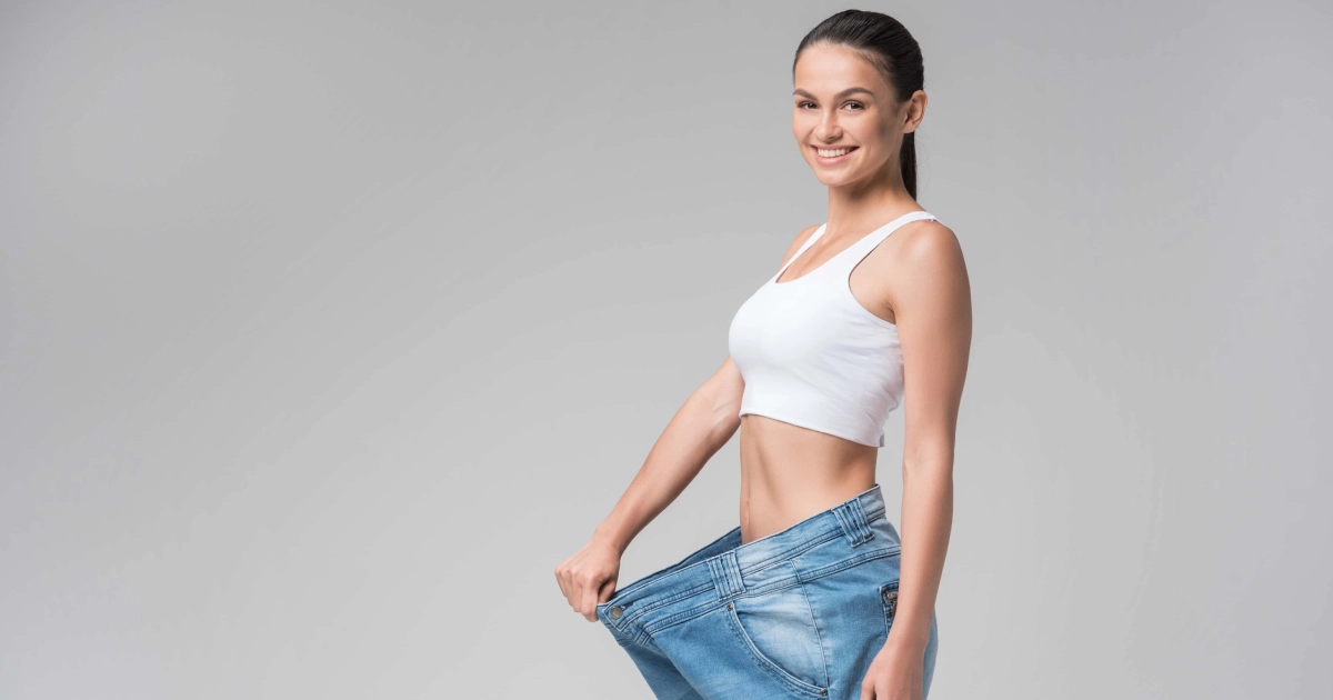 Woman showing significant weight loss by holding out oversized jeans, after Fat Loss Treatment in Harbor City, CA